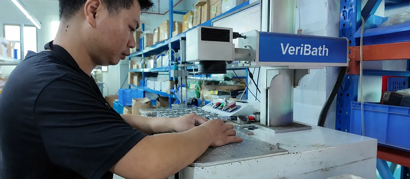 VeriBath worker operating laser-marking equipment at a factory inspection station